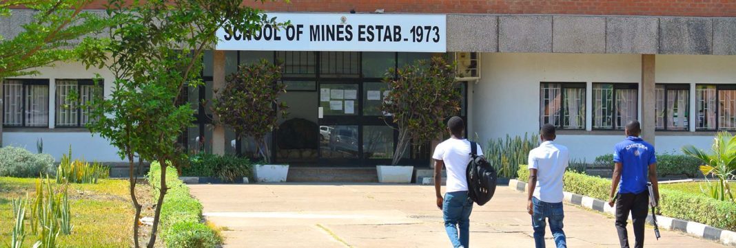 a picture of 3 maile zambia students walking up to the entrance of the school of mines which was established in 1973