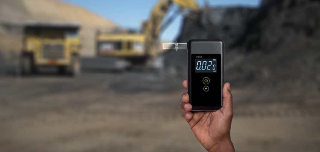 Man holding a breathalyzer tester in an open pit mining environment