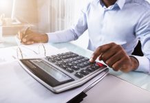Close-up Of A Businessman Calculating Invoice Using Calculator At Workplace