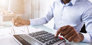 Close-up Of A Businessman Calculating Invoice Using Calculator At Workplace